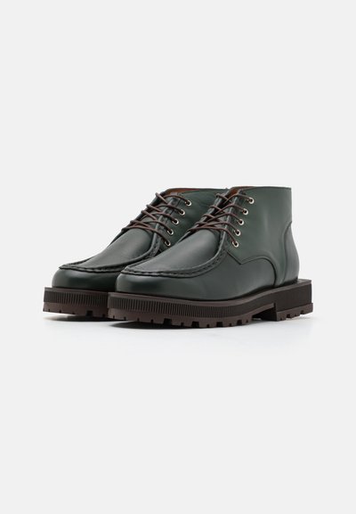 Green leather ankle boots featuring rounded toes, brown laces, and textured rubber soles with ridges. Stitch detailing around edges.