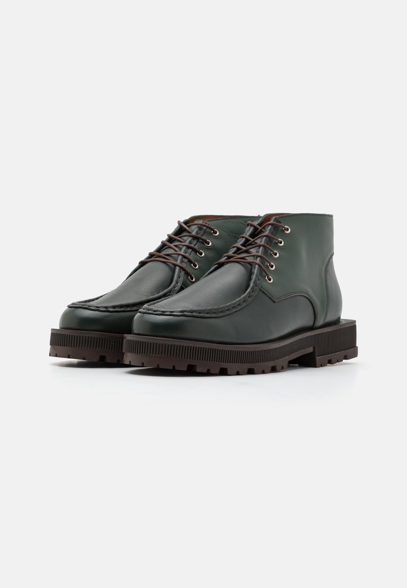 Grüne Leder-Stiefeletten mit runden Zehen, braunen Schnürsenkeln und strukturierten Gummisohlen mit Rillen. Steppnähte entlang der Kanten.
