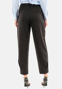 Pantaloni neri con una vestibilità su misura, parte anteriore liscia, tasche posteriori e una texture morbida. Indossati con scarpe con tacco alto.