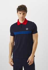 Tengerészkék póló piros gallérral, kék vízszintes csíkokkal és egy kis logóval a mellkason. Pamutból készült, klasszikus szabással.