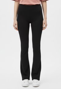 Leggings neri svasati realizzati in materiale elasticizzato, con design a vita alta. Indossati con scarpe da ginnastica bianche e una maglia rosa ampia.