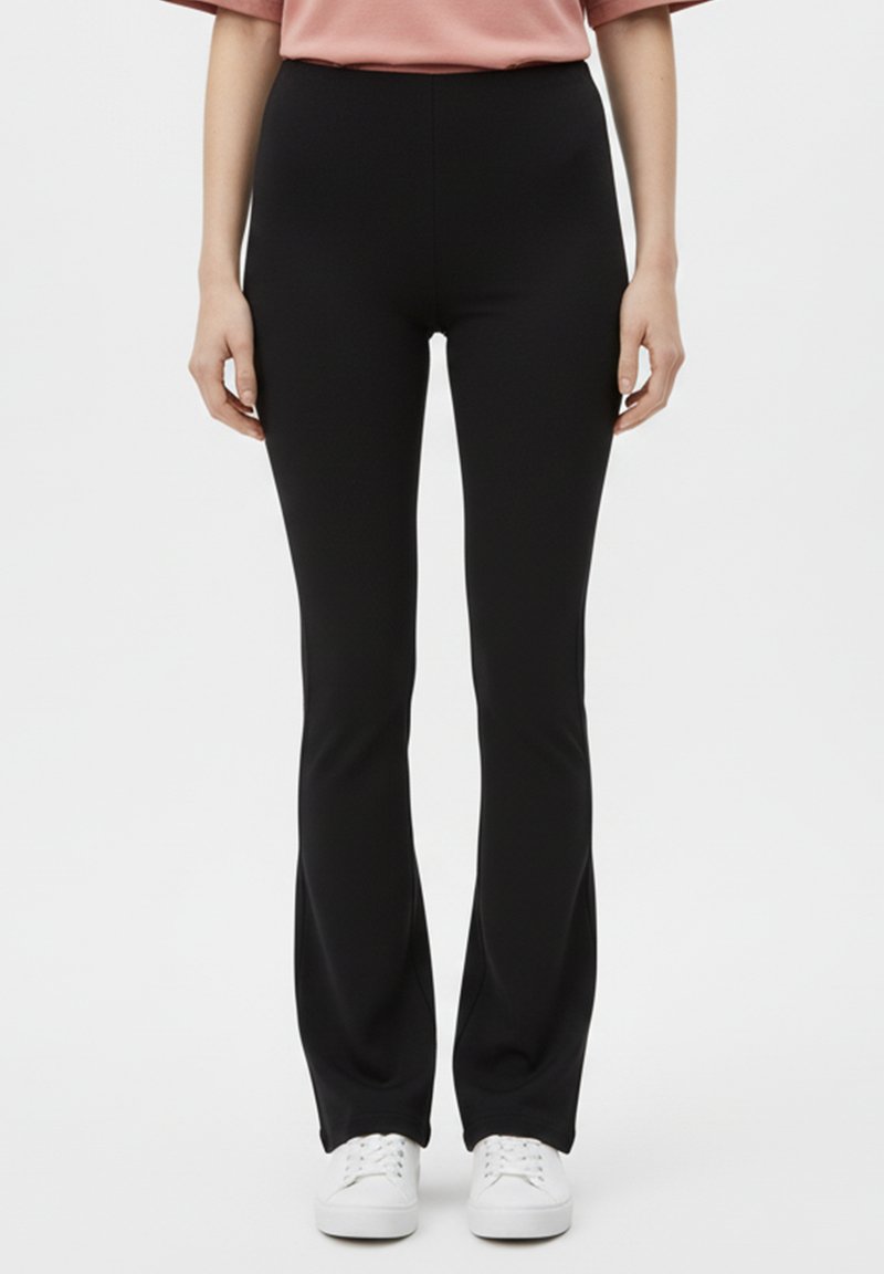 Leggings neri svasati realizzati in materiale elasticizzato, con design a vita alta. Indossati con scarpe da ginnastica bianche e una maglia rosa ampia.