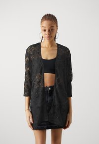 Black lace kimono cardigan with 3/4 sleeves, open front design, intricate patterns, and a lightweight texture. Worn over a black crop top.