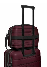 Bordeauxkleurige harde bagageset met een uitklapbare zwarte handgreep. De bovenste tas is vastgemaakt met een zwarte strap en heeft een textuur op het oppervlak.