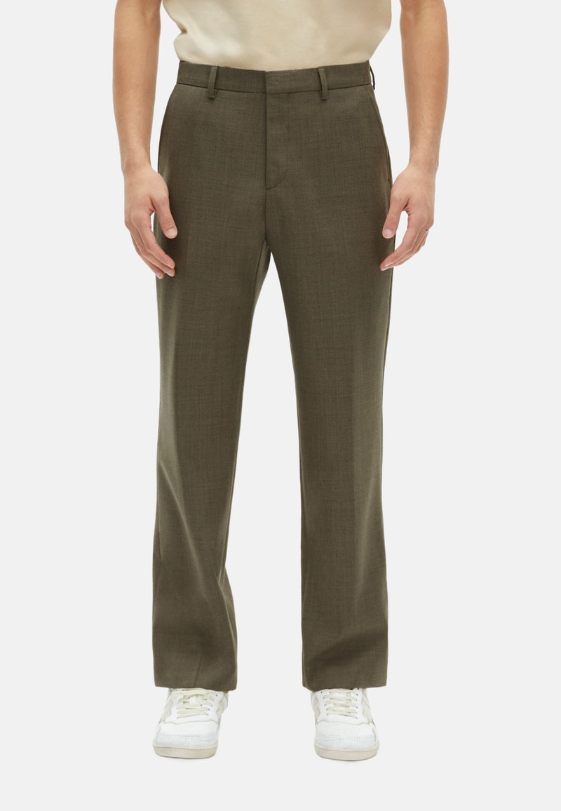 Pantalones verde oliva con una textura suave, diseño de corte recto, bolsillos frontales y pasadores para cinturón, combinados con zapatillas blancas.