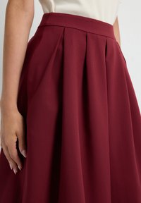 Jupe plissée bourgogne, confectionnée en tissu doux. Dotée d'une taille ajustée et d'un design fluide et texturé tout au long.