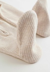 Zbliżenie na beżowe, prążkowane skarpety dzianinowe rozłożone płasko na białej powierzchni, ukazujące fakturę tkaniny i obszary pięty.