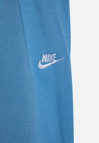 Zila kokvilnas T-krekls ar baltu izšuvumu Nike logotipu kreisajā krūšu daļā. Audumam ir gluda tekstūra un tas ir viegls.