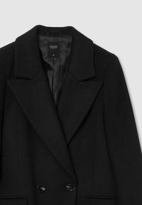 Cappotto in misto lana nero con colletto a punte, chiusura doppiopetto e grandi bottoni neri. Presenta tasche laterali e una morbida fodera interna.