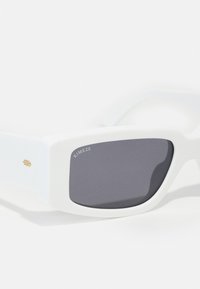Gafas de sol blancas con montura rectangular, lentes gris oscuro y un acento dorado en la patilla. Textura suave y diseño minimalista.