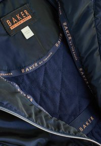 Interno della giacca imbottita navy con texture satinata, che presenta il marchio "BAKER by Ted Baker" in rame sul tessuto e sulla custodia della cerniera.