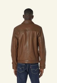 Bruine leren jas met een gladde textuur en een klassieke kraag, met een rechte snit en stiksel details. Gedragen over een blauwe jeans.