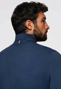 Navy blue paita korkealla kauluksella, joka on valmistettu sileästä kankaasta. Kauluksen lähellä on pieni punainen, valkoinen ja sininen yksityiskohta. Tiukka istuvuus.