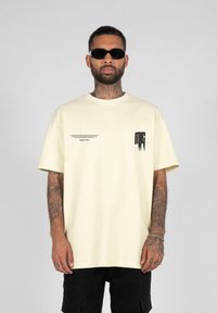 Cream-colored oversized T-shirt with short sleeves, featuring a black graphic print on the left chest and left side text detail.