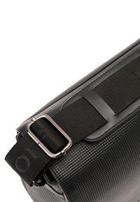 Schwarze Umhängetasche aus strukturiertem Material, mit verstellbarem Stoffgurt, metallischer Schnalle und glatten Akzenten entlang der Kanten.