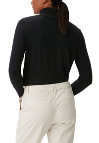Schwarzer Rollkragenpullover mit schmaler Passform, ausgestattet mit glatter Textur und minimalen Nähten, kombiniert mit beigen Hosen, die Seitentaschen haben.