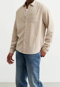 Beige pitkähiha paita, jossa nappikaulus, edessä tasku ja pehmeä materiaali. Yhdistetty kulutettuihin sinisiin farkkuihin.