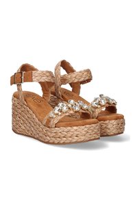 Sandalias de cuña con fibras naturales trenzadas, tonos beige, correa de tobillo ajustable y acentos decorativos de piedras de cristal claras en la parte delantera.