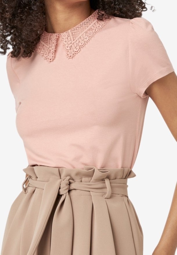 Kortärmad rosa topp med spetskrage, i kombination med en beige hög midja kjol med knytning i midjan och veckdetaljer.