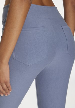 Nahaufnahme des unteren Rückens und der Hüften einer Person, die hochgeschnittene, hellblaue, figurbetonte Hosen mit Gesäßtaschen und sichtbaren Nähten trägt.