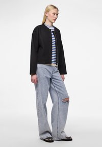 Veste noire cropped avec une fermeture éclair à l'avant, portée sur un pull rayé bleu et blanc, associée à un jean large déchiré bleu clair.