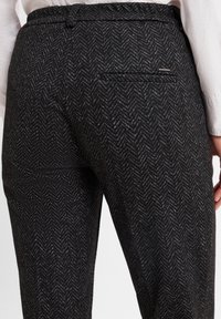 Schwarze Hosen im Fischgrätmuster mit glatter Textur, ausgestattet mit einem elastischen Bund und einer einzelnen Gesäßtasche für Funktionalität.