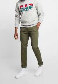 Grauer Hoodie mit mehrfarbigem "GAP"-Logo, olivgrüne Hose und weiße Sneaker. Lässiger Look mit gerippten Bündchen und einer Fronttasche.