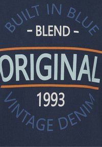 Donkerblauwe stof met wit, lichtblauw en oranje bedrukt tekst; luidt "Original Blend - Built in Blue Vintage Denim 1993".