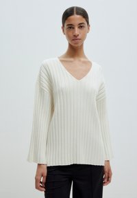 White ribbed knit sweater with a V-neck, relaxed fit, and long sleeves featuring a textured surface and slight fraying at the hem.