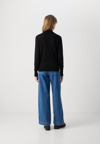 Svart stickad tröja med hög krage, i kombination med löst sittande blå jeans. Outfitten har en klassisk skärning och en avslappnad känsla.