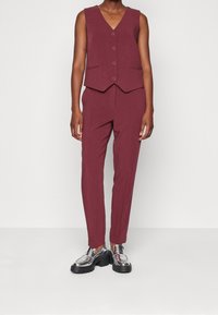 Mörkröd väst med V-urringning och fem knappar, tillsammans med matchande tapered byxor. Metalliska platåskor fulländar looken.