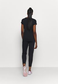 Svart kortärmad topp och matchande joggersbyxor med en åtsittande design. Modellen bär ljusrosa träningsskor med en strukturerad sula.