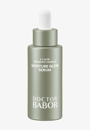 Flacon de sérum en verre vert avec un capuchon compte-gouttes blanc. L'étiquette présente "Complexe Postbiotique à 6% Aloe" et "Sérum Éclat Hydratant" en texte blanc.