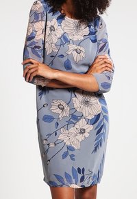 Floral print dress in light blue fabric, featuring three-quarter sleeves, a round neckline, and detailing of large beige and blue flowers.