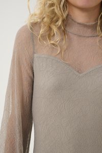 Gray lace top with long, sheer sleeves and a scalloped neckline. Intricate floral pattern and textured fabric create a layered appearance.
