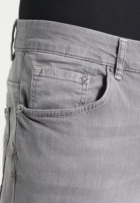Pantaloni in denim grigio con un classico design a cinque tasche, cuciture visibili e un dettaglio in metallo argentato in vita. Texture liscia.