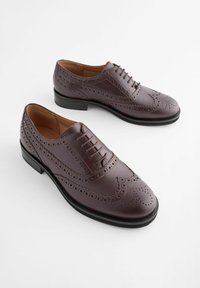 Chaussures brogue en cuir marron avec un design à bout d'aile, un détail perforé, un bout rond et une semelle plate en caoutchouc noir. Comprend des lacets et une texture lisse.