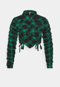 Camicia corta a quadri verdi e neri con un davanti bottonato, maniche lunghe arricciate e dettagli a lacci in vita e sulle maniche.