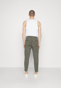 Pantalons en coton verts avec un design fuselé, taille élastique et deux poches arrière, associés à un débardeur blanc et des baskets blanches.