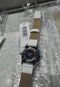 Silberne Armbanduhr aus Edelstahl mit rundem Zifferblatt, weißem Lederarmband und schwarzem Zifferblatt. Rückseite mit der Aufschrift „Designed by Regal Sweden“. Zeitmarkierungen fehlen.