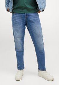 Lichtblauwe denim jeans met een rechte snit, voorzien van vijf zakken en subtiele vervaging. Gepaard met witte sneakers op een neutrale achtergrond.