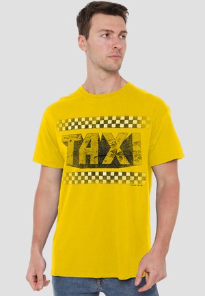 Yellow cotton t-shirt featuring a large black "TAXI" print surrounded by a black and yellow checkered pattern. Short sleeves, round neckline.