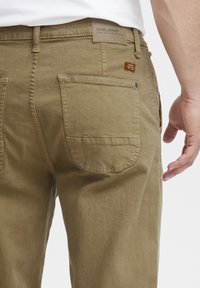 Chinos khaki con taglio dritto, dotati di due tasche posteriori, un'etichetta con logo Blend e dettagli di cucitura sottili sui bordi delle tasche.