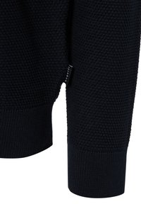 Granatowy sweter dzianinowy z fakturowanym wzorem, ściągaczami na mankietach i boczną metką. Materiał wydaje się miękki i ciepły, odpowiedni na chłodną pogodę.