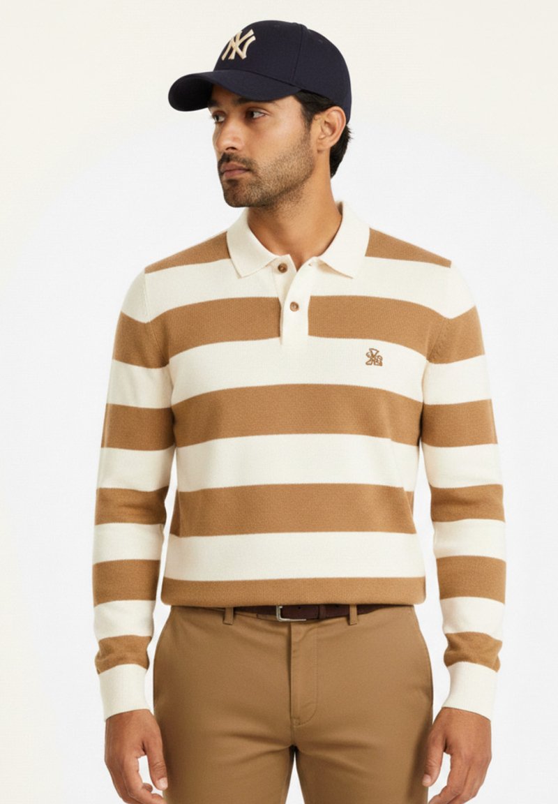 Suéter a rayas en beige y marrón claro con cuello, que presenta un logotipo en el pecho. Combinado con pantalones color cuero y una gorra azul marino.