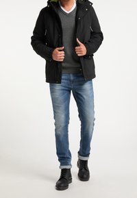 Veste noire à capuche avec une texture lisse, pull gris, jean bleu et bottes noires à lacets. La veste comporte des fermetures éclair et une doublure verte contrastante.