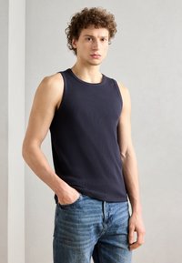 Top din bumbac ribbed de culoare bleumarin, cu guler rotund, purtat cu blugi de culoare albastru deschis. Țesătura pare netedă, iar croiala este ajustată, fără modele.