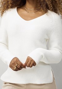 White knitted sweater with a V-neck, long sleeves, and ribbed texture. Features side slits at the hem for a relaxed fit.