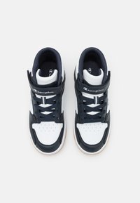 White and navy high-top sneakers with perforated toe, padded collar, lace-up front, and velcro strap. Features Champion logo on side.