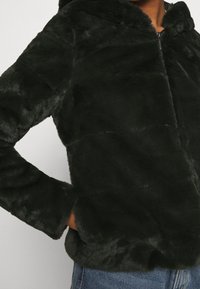 Ciemnozielona bluza z futra syntetycznego z kapturem, z zamkiem błyskawicznym z przodu, teksturowanym materiałem i prostokątnym krojem.
